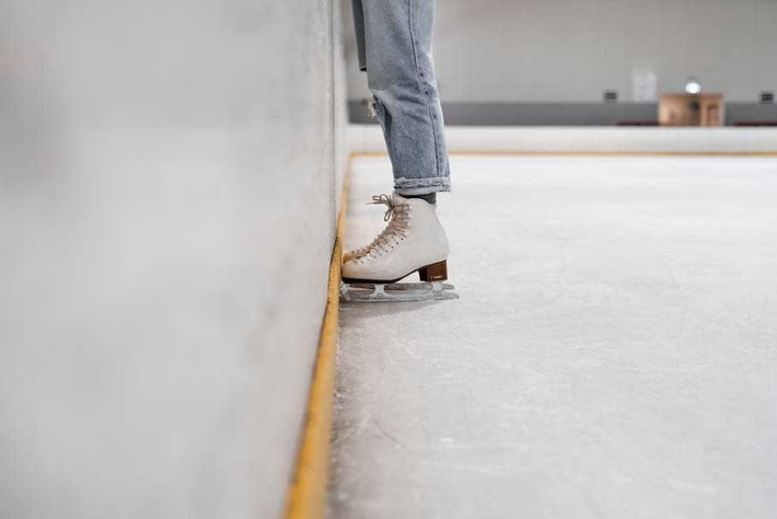 Person wearing white and gray skate shoes inside ice skating rink